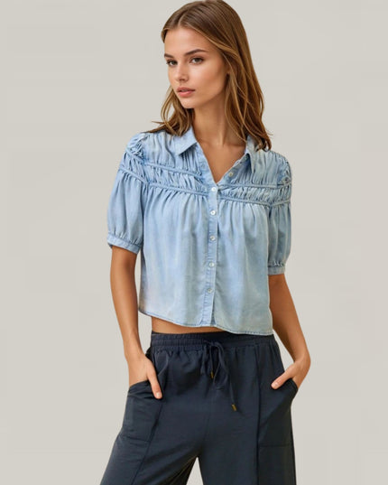 Woman wearing a light blue denim shirt and dark pants on a plain background