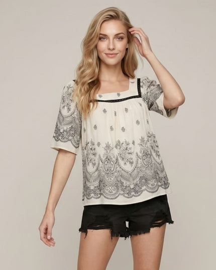 Woman wearing a white blouse with black lace details and black shorts on a beige background