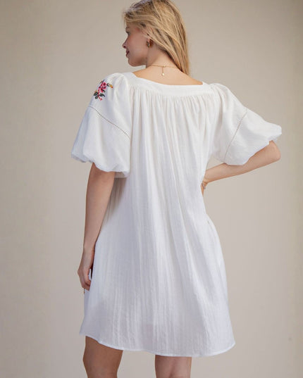 Woman wearing a white dress with floral embroidery on a beige background
