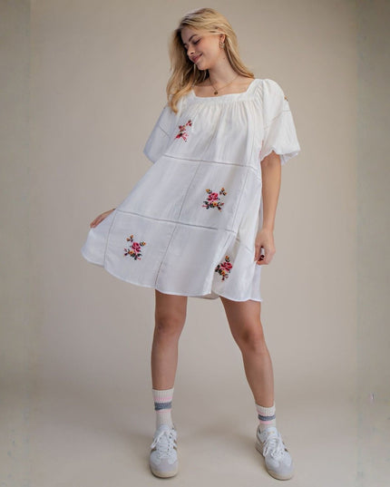 Woman wearing a white dress with floral embroidery against a beige background