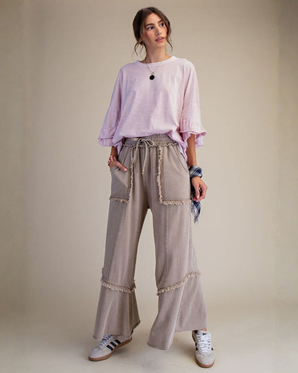 Woman wearing a light pink top and beige pants against a plain background
