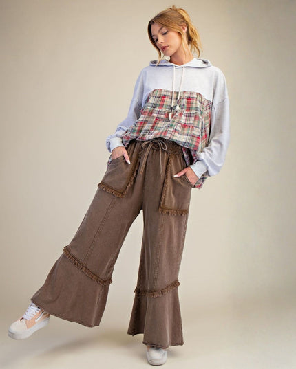 Woman wearing a plaid top and brown wide-leg pants against a neutral background