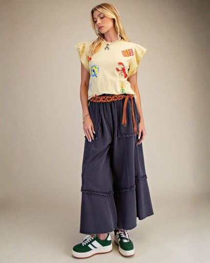 Woman wearing a colorful top and wide-leg pants with a brown belt against a neutral background