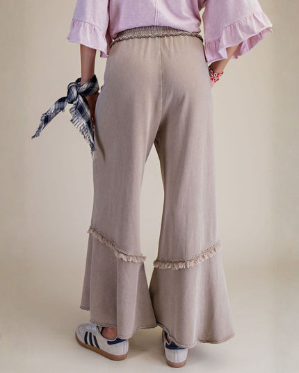 Person wearing beige flared pants with ruffled hem on a plain background