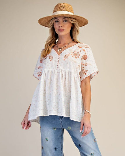 Woman wearing a white embroidered top and blue jeans with a straw hat on a beige background