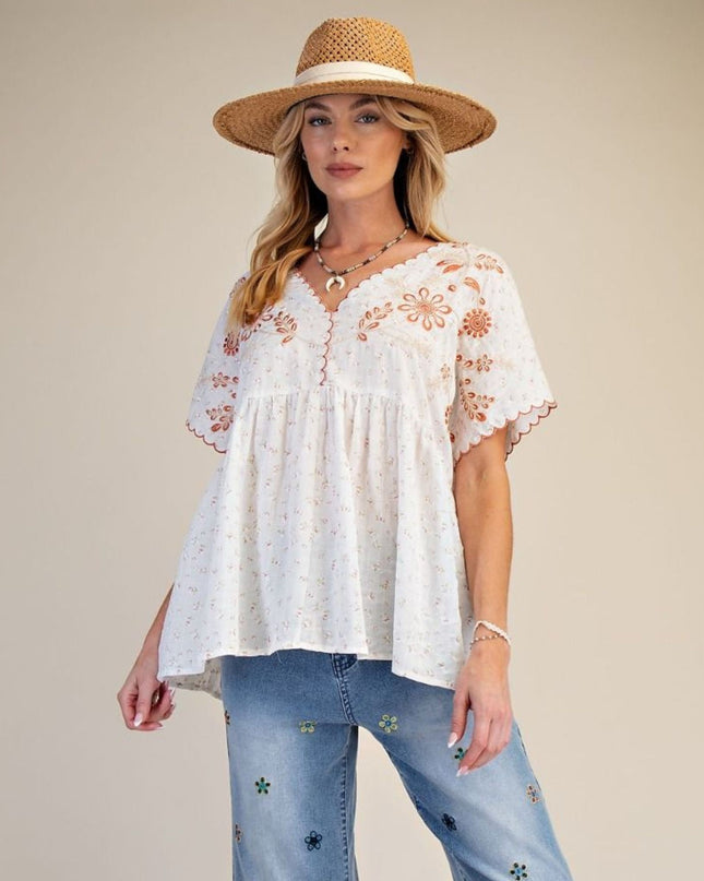 Woman wearing a white embroidered top and blue jeans with a straw hat on a beige background
