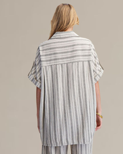 A woman shown from the back wearing a loose, short-sleeve striped shirt and matching striped pants against a plain beige studio background.