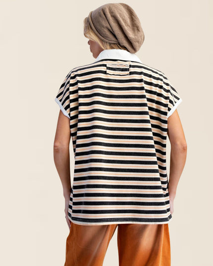 A woman shown from behind wearing a short-sleeve striped polo shirt with black and beige horizontal stripes, paired with brown pants and a brown headscarf, against a solid light beige background.