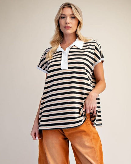 A woman modeling a short-sleeve polo shirt with black and off-white horizontal stripes, paired with brown pants, against a plain beige studio background.