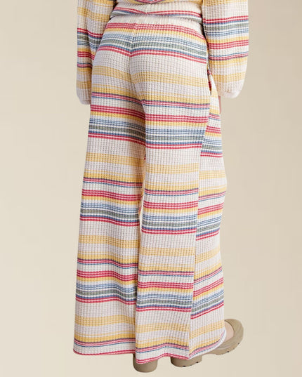A person shown from the back wearing wide-leg striped pants and a matching striped top, photographed against a plain warm beige studio background.