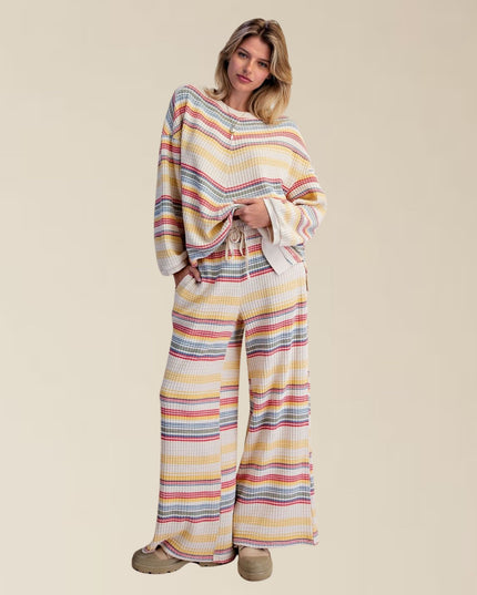 A woman modeling a matching two-piece lounge set with a waffle-knit texture and horizontal multicolor stripes in yellow, pink, blue, and green on a cream base, set against a solid beige background.