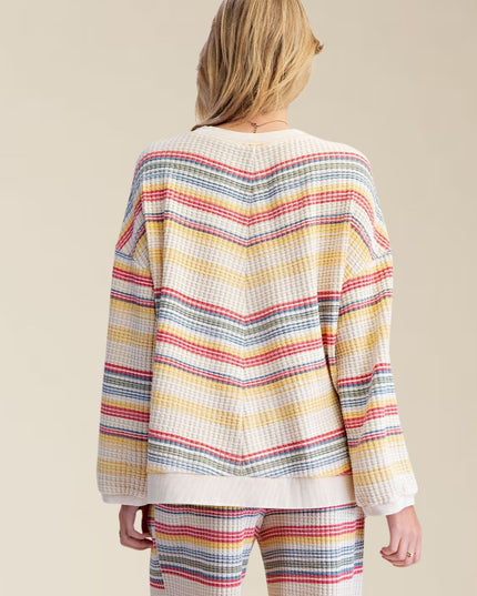 A woman shown from the back wearing a waffle-knit long-sleeve sweater and matching striped pants in a cream base with multicolor chevron stripes.