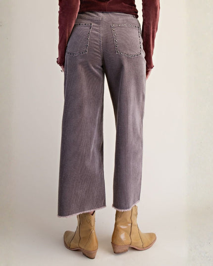A person shown from the back wearing wide-leg cropped pants in a muted mauve-gray corduroy fabric with frayed hems, paired with tan ankle boots and a burgundy top, against a plain off-white studio background.