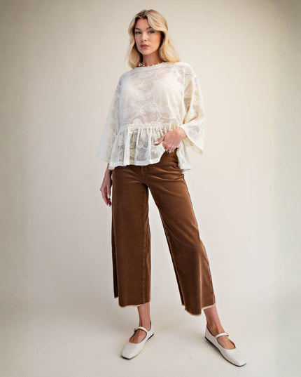 A woman modeling a white lace long-sleeve blouse with a ruffled hem and brown wide-leg cropped pants, paired with white Mary Jane shoes, against a neutral studio backdrop.