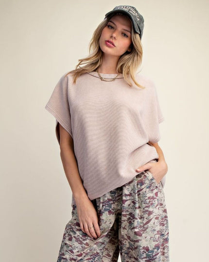 A woman modeling a light pink ribbed knit t-shirt and patterned wide-leg pants against a solid beige studio background.