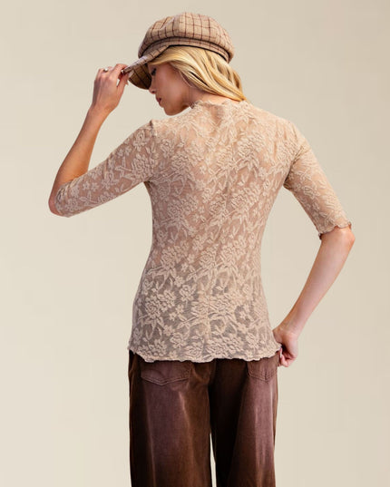 A woman shown from the back wearing a beige lace three-quarter sleeve top, brown wide-leg pants, and a brown plaid flat cap, set against a solid light beige background.
