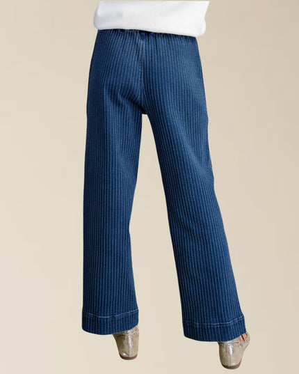 A pair of wide-leg blue jeans with a vertical pinstripe pattern, shown on a model from the back against a solid beige background.