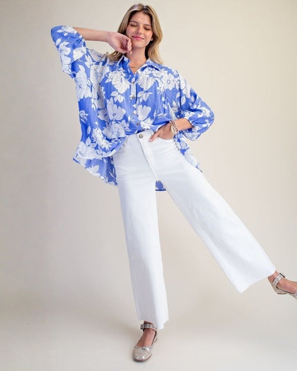 A woman modeling a blue and white floral long-sleeve button-up shirt paired with white wide-leg pants and silver flat shoes, posed against a solid light beige studio background.