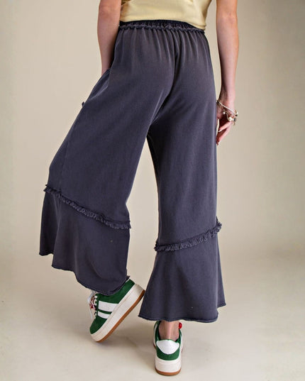 Navy blue wide-leg pants with ruffled edges worn by a person on a beige background