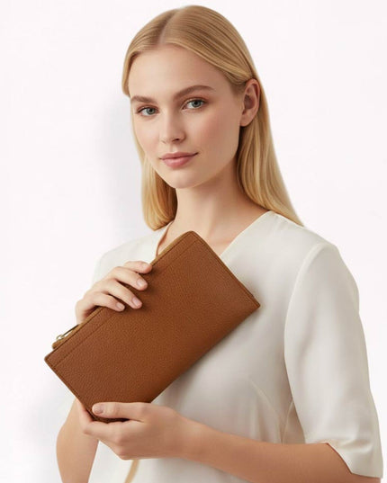 A blonde woman wearing a white blouse holds a brown textured leather clutch bag against a clean white background.