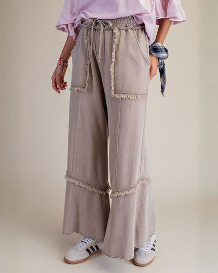 Person wearing beige wide-leg pants with ruffled details on a plain background