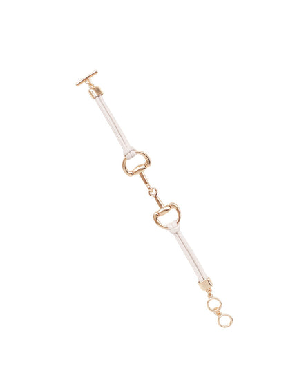 A delicate equestrian-style bracelet featuring a white leather strap and polished gold-tone metal hardware, including a horsebit motif and snap closure, set against a solid white background.