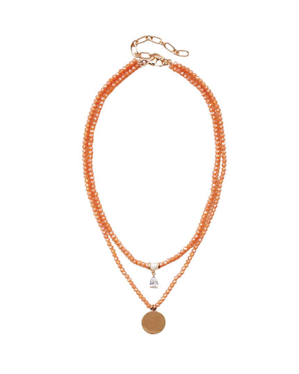 A double-strand beaded necklace in a warm peach-orange color with a small silver-toned charm and a round gold-toned disc pendant, displayed on a clean white background.
