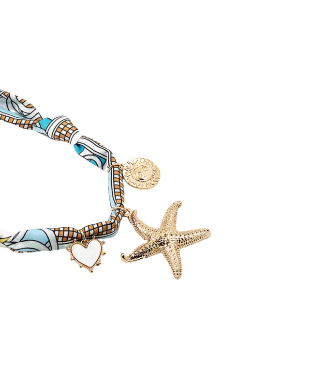 A close-up of a jewelry accessory set featuring a patterned fabric strap with turquoise, white, and brown motifs, gold-toned charms including a starfish, a heart outline, and a round medallion, on a plain white background.