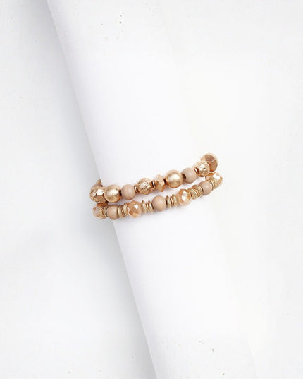 Two beaded stretch bracelets in a champagne gold and beige tone, displayed on a white cylindrical stand against a white background.