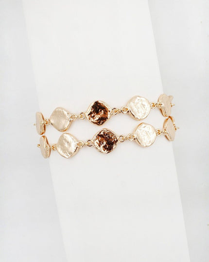 A double-strand gold-tone bracelet featuring textured, irregular disc-shaped beads, with two central dark brown faceted gemstone accents, displayed on a white cylindrical stand.
