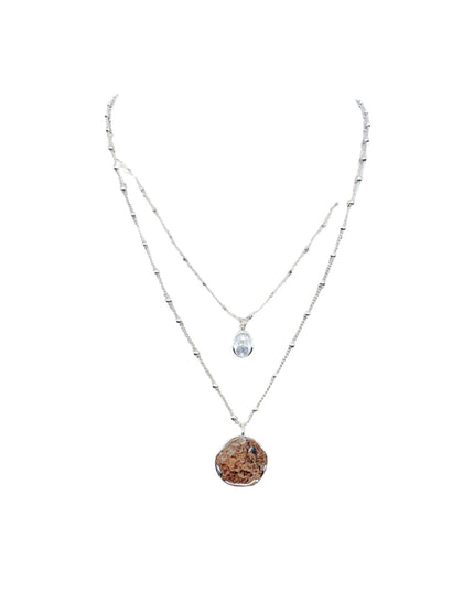 A double-strand silver necklace featuring a long chain with small metallic beads and a shorter chain with a clear teardrop crystal pendant and a larger irregular brown stone pendant, displayed on a solid white background.