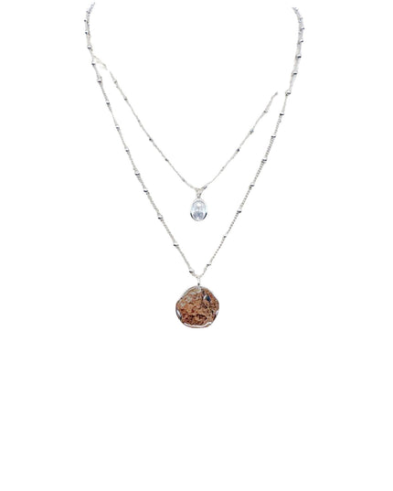 A double-strand silver necklace featuring a long chain with small metallic beads and a shorter chain with a clear teardrop crystal pendant, paired with a longer pendant made of a textured brown and gold stone, shown on a plain white background.