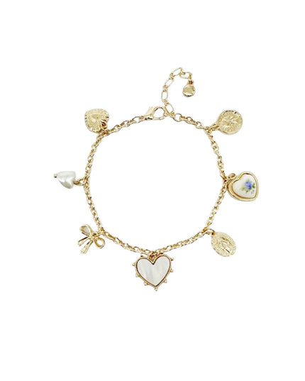 A delicate gold-tone charm bracelet featuring multiple heart-shaped charms, including a central heart with a white inlay, a small heart with blue floral details, and textured gold disc charms, displayed on a clean white background.