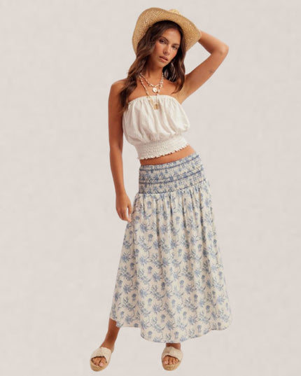 Woman wearing a white top and floral skirt with a straw hat on a plain background