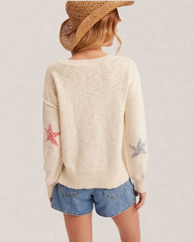 Person wearing a cream sweater with star designs and denim shorts on a plain background