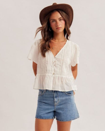 Woman wearing a white blouse and denim shorts with a brown hat on a plain background