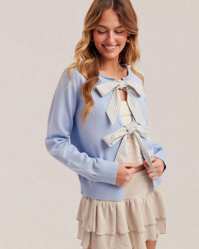 Woman wearing a light blue sweater with a bow detail and a beige skirt on a plain background