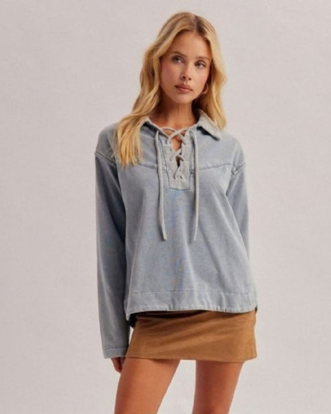 A woman modeling a light blue denim long-sleeve top with a lace-up neckline, paired with a brown mini skirt, against a plain light gray studio background.
