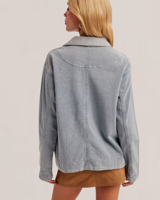 A woman shown from the back wearing a light gray washed denim jacket and a brown mini skirt, set against a plain light beige studio background.