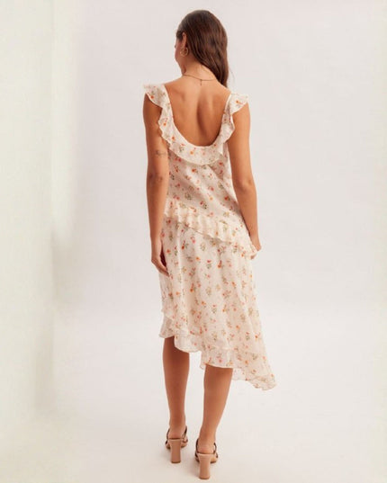 A woman viewed from behind wearing a ruffled back dress with a small floral print, paired with beige high-heeled sandals, set against a plain white studio background.