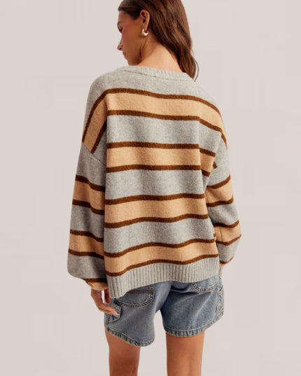 A woman shown from the back wearing a loose-fit knit sweater with horizontal stripes in light gray, beige, and brown, paired with denim shorts against a plain light gray studio background.