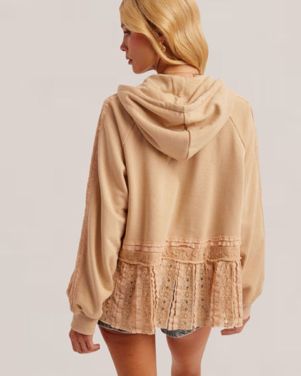A woman shown from the back wearing a beige hooded sweatshirt with a lace ruffle hem detail, paired with denim shorts, against a plain light gray studio background.
