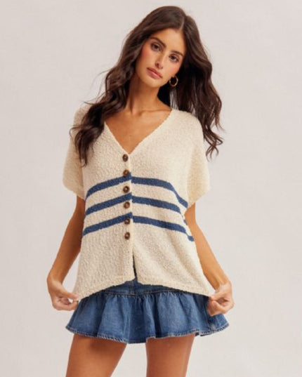Woman wearing a white cardigan with blue stripes and brown buttons, paired with a denim skirt on a plain background.