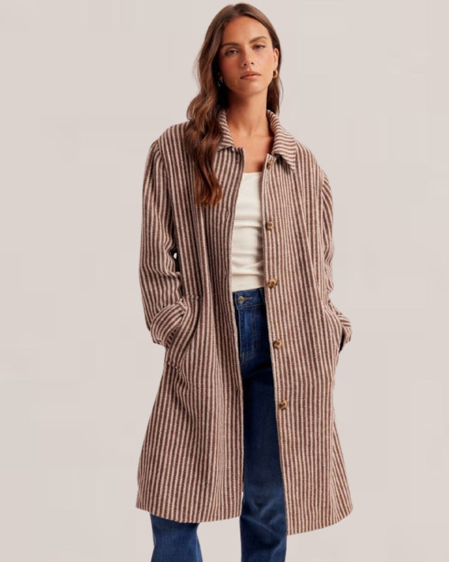 A woman modeling a mid-length brown and beige vertically striped wool-blend coat over a white top and blue jeans, photographed against a plain light gray studio background.