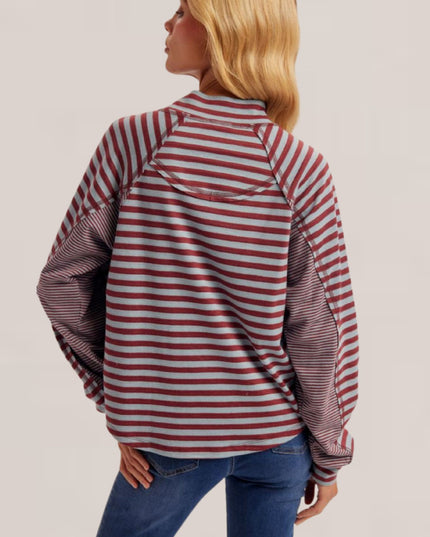 A woman shown from the back wearing a long-sleeve raglan-style top with red and white horizontal stripes on the body and darker striped sleeves, paired with blue jeans, against a plain light beige studio background.