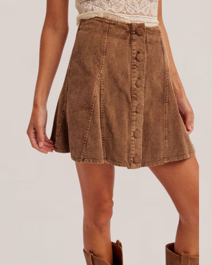 A brown corduroy mini skirt with a button-front closure, modeled with a cream lace top and brown boots against a light beige studio background.