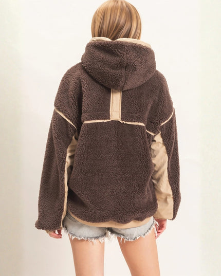 A person shown from the back wearing a brown sherpa fleece hooded jacket with beige contrast panels and denim shorts against a plain light background.