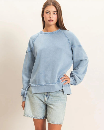 A woman modeling a light blue washed sweatshirt with matching light blue denim shorts against a plain off-white studio background.
