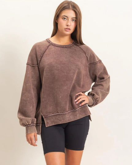 A woman modeling a washed brown long-sleeve sweatshirt with elasticized cuffs and hem, paired with black biker shorts, against a plain off-white studio background.