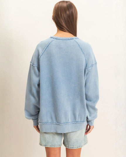 A woman viewed from behind wearing an oversized light blue washed sweatshirt and matching denim shorts against a plain off-white background.